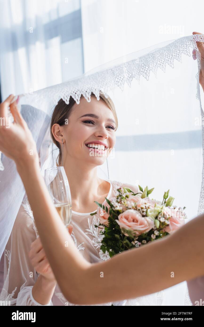bridesmaid holding veil of joyful bride with wedding bouquet and champagne  Stock Photo - Alamy