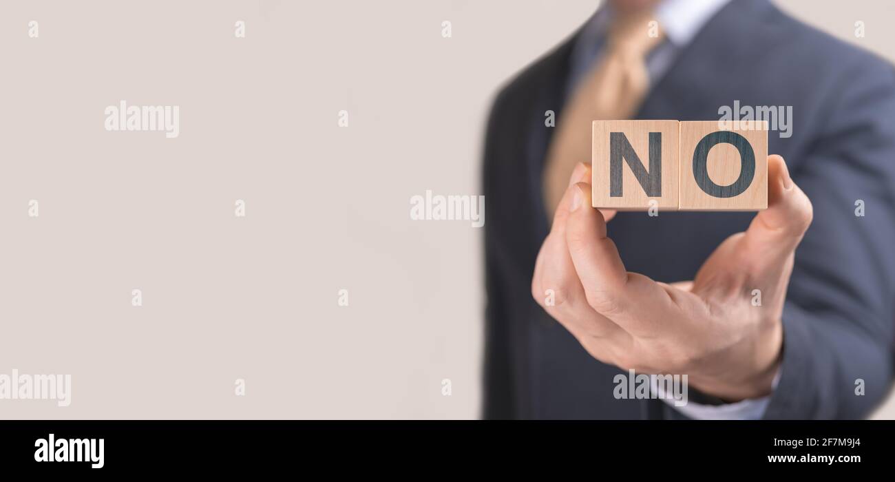 Businessman show wording NO on wooden cubes. Negative answer concept. No risk, refusal to hire concept. Man in a suit hold NO text on cubes. banner, c Stock Photo