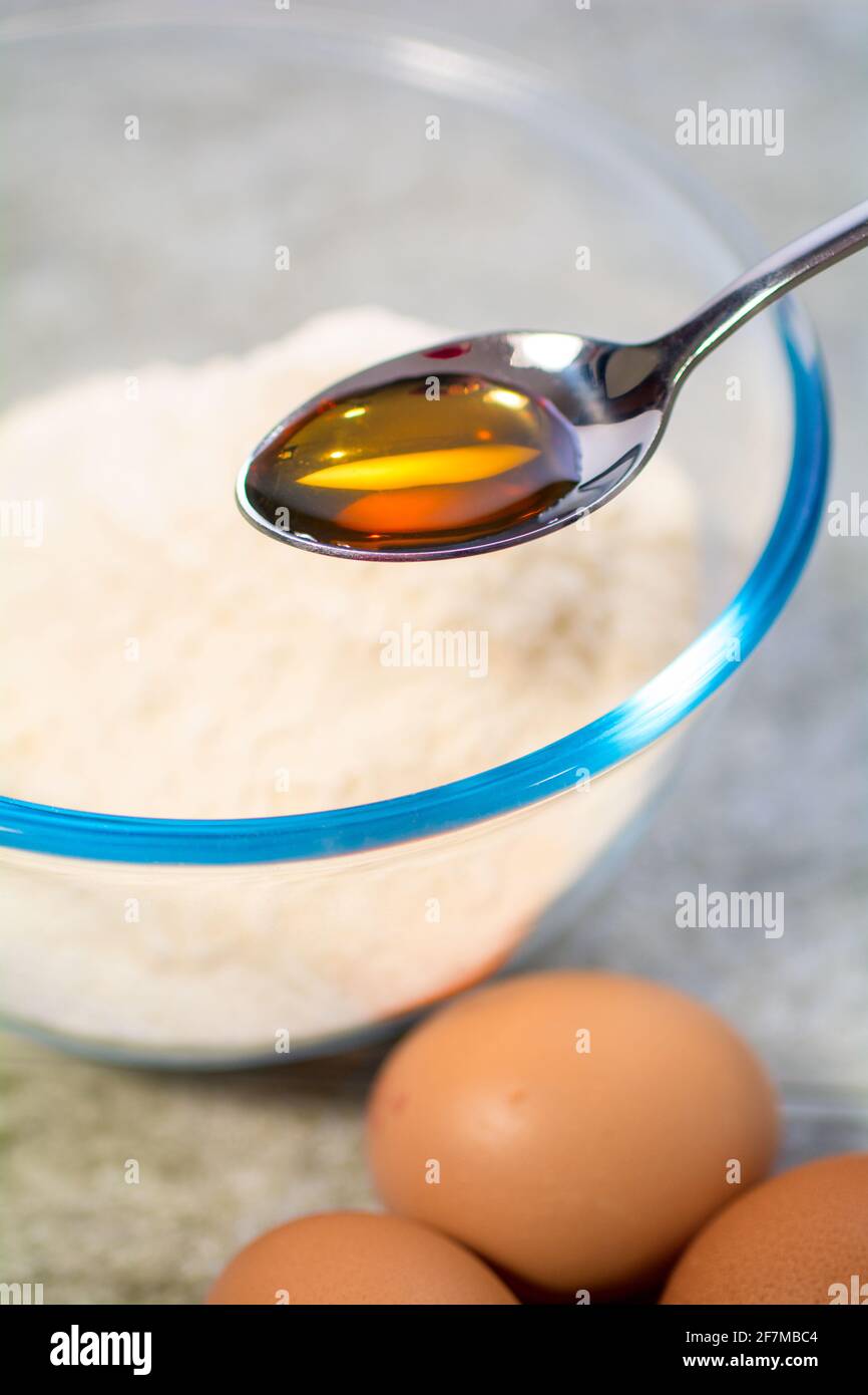A teaspoon of vanilla extract about to be poured into a cake mix Stock Photo