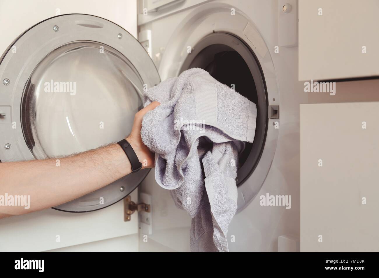 Man loading color clothes and towels into built-in washing machine Stock Photo