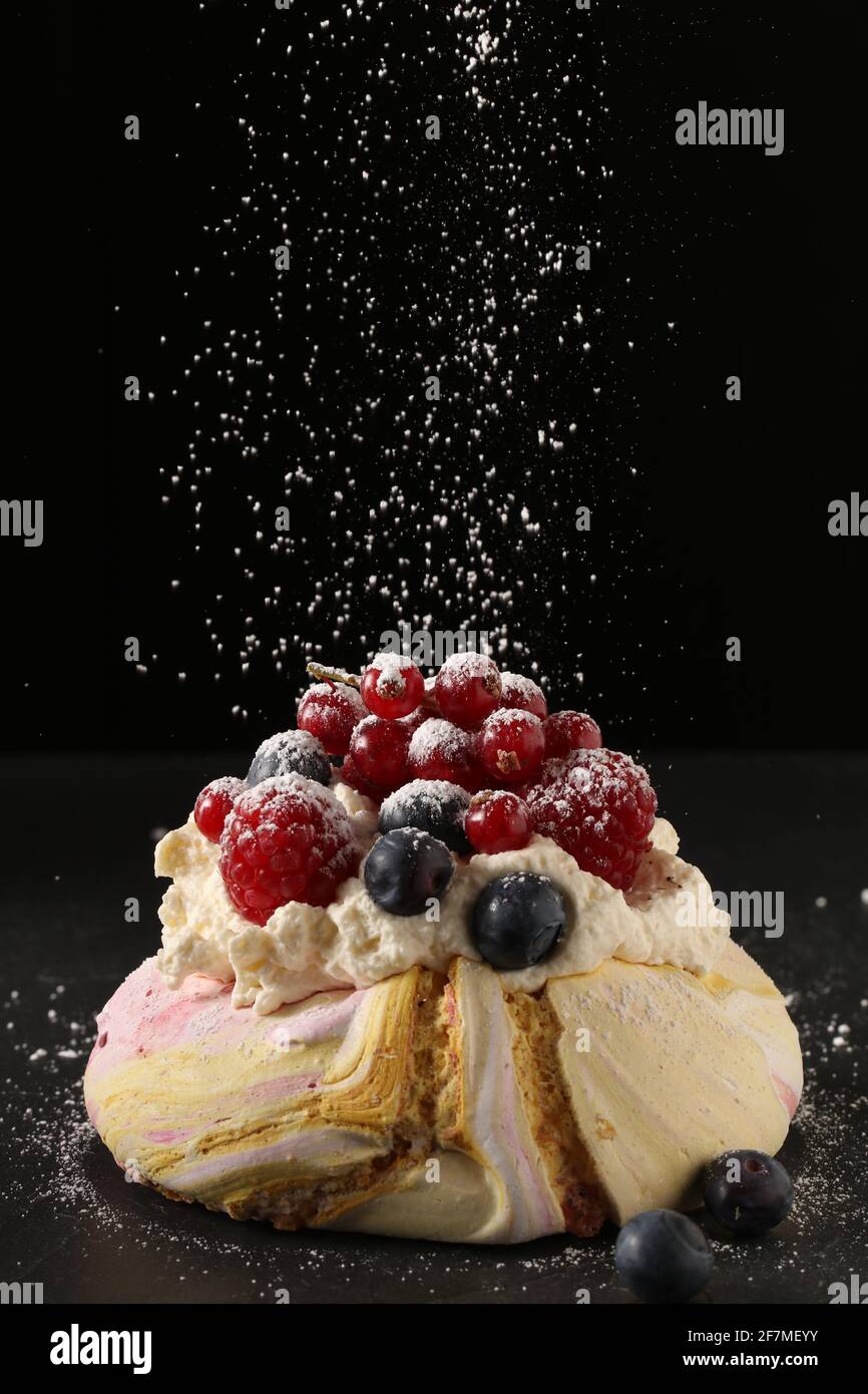 Raspberries, blueberries, redcurrants with cream on a multi coloured meringue base with icing sugar coating Stock Photo