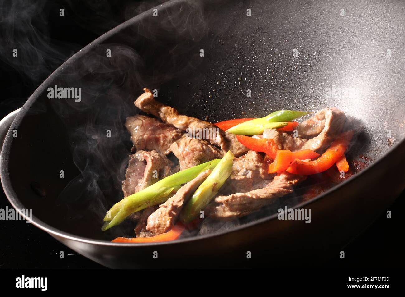 https://c8.alamy.com/comp/2F7MF0D/meat-cooking-in-a-large-frying-pan-with-spring-onions-and-red-peppers-with-steam-coming-off-2F7MF0D.jpg