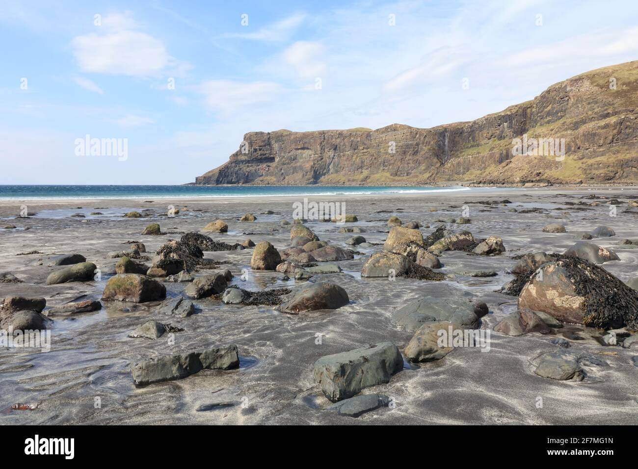 View across beach with large rounded rocks, wave breaking, sea cliff ...