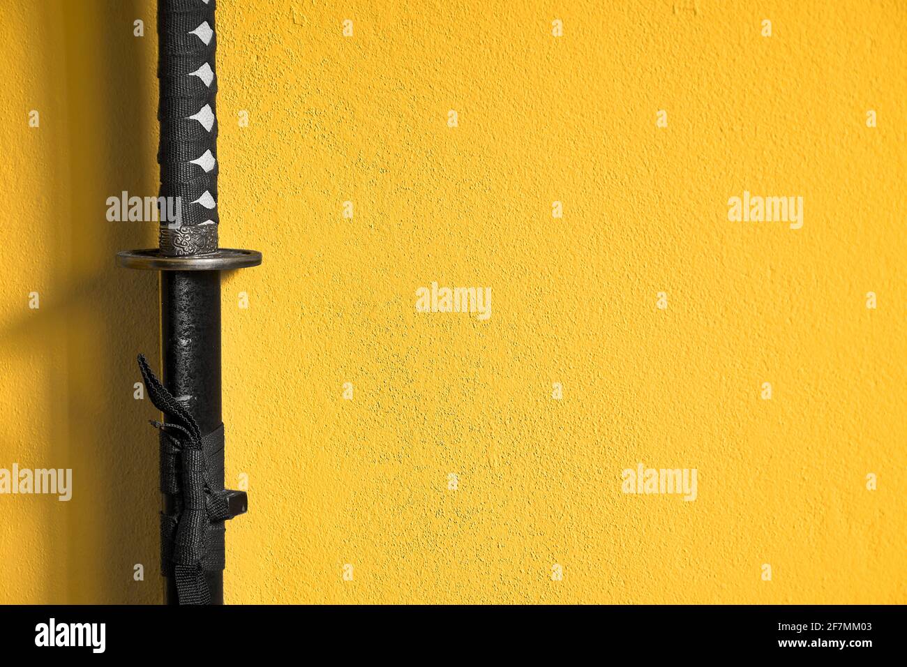 Closeup of Japanese sword katana in scabbard isolated on yellow background wall. Sword used for martial arts such as kenjutsu, ninjutsu and battojutsu Stock Photo