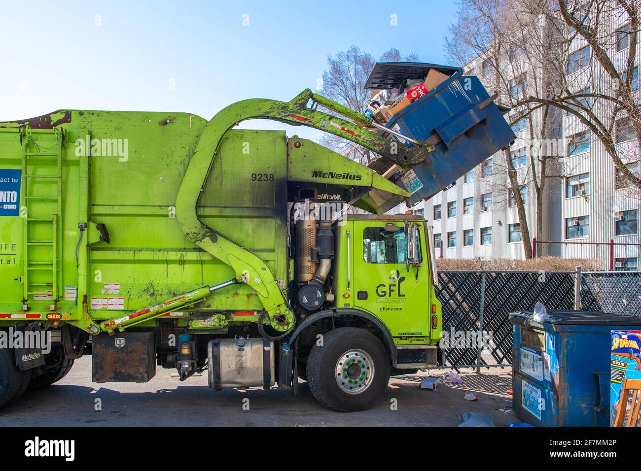 Recyclable garbage pick-up truck and service in the Toronto city. A GFL branded vehicle lifts a large metallic container from an apartment building Stock Photo