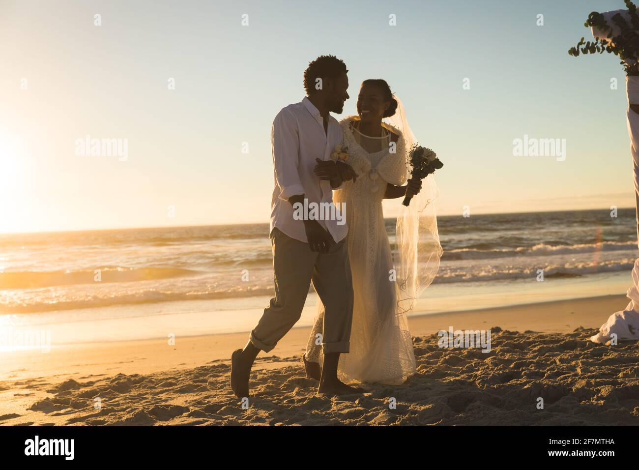 African american couple in love getting married, walking on beach holding hands at sunset Stock Photo