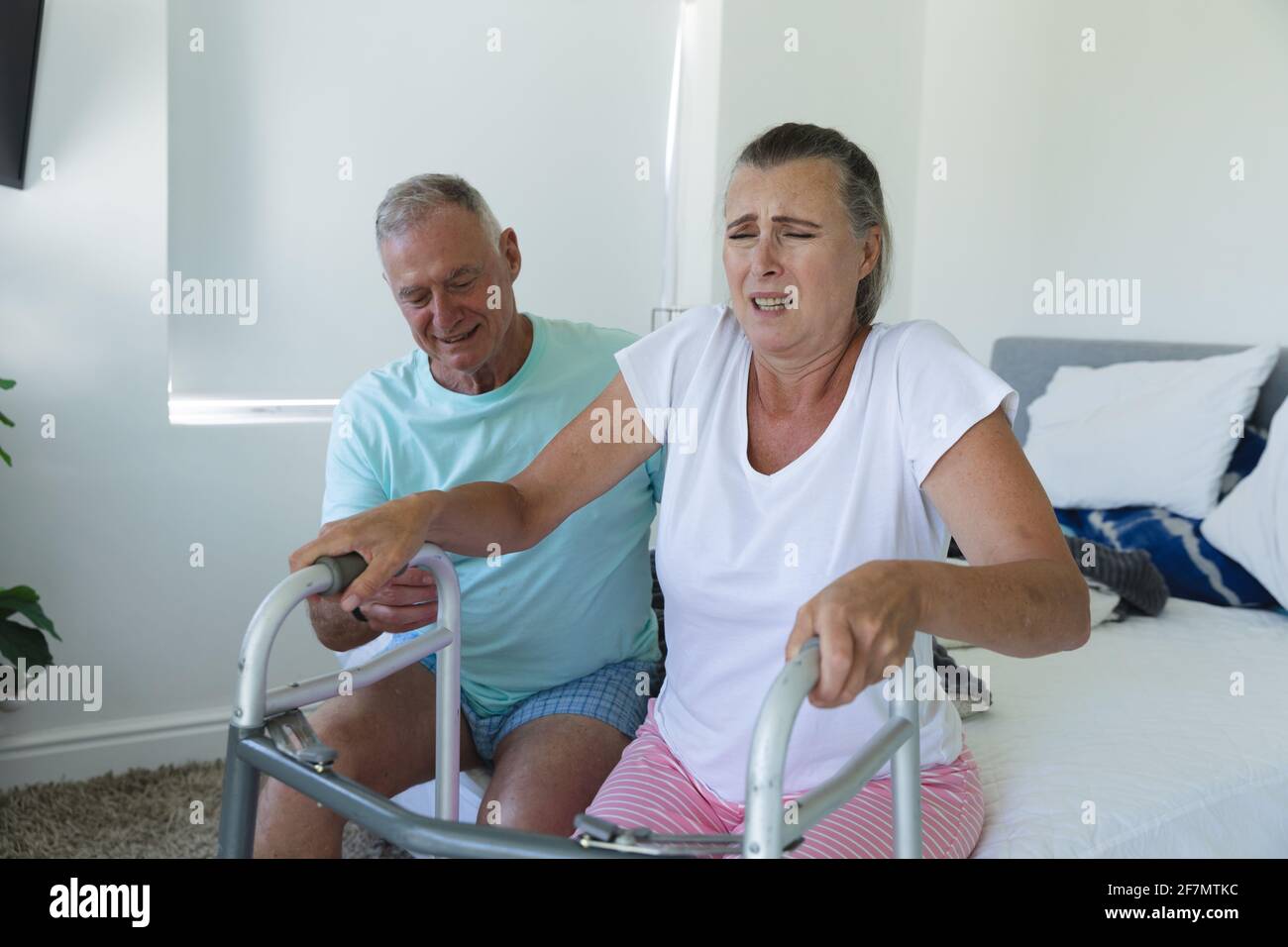 Caucasian Senior Couple Sitting On Bed Husband Helping Wife Stand