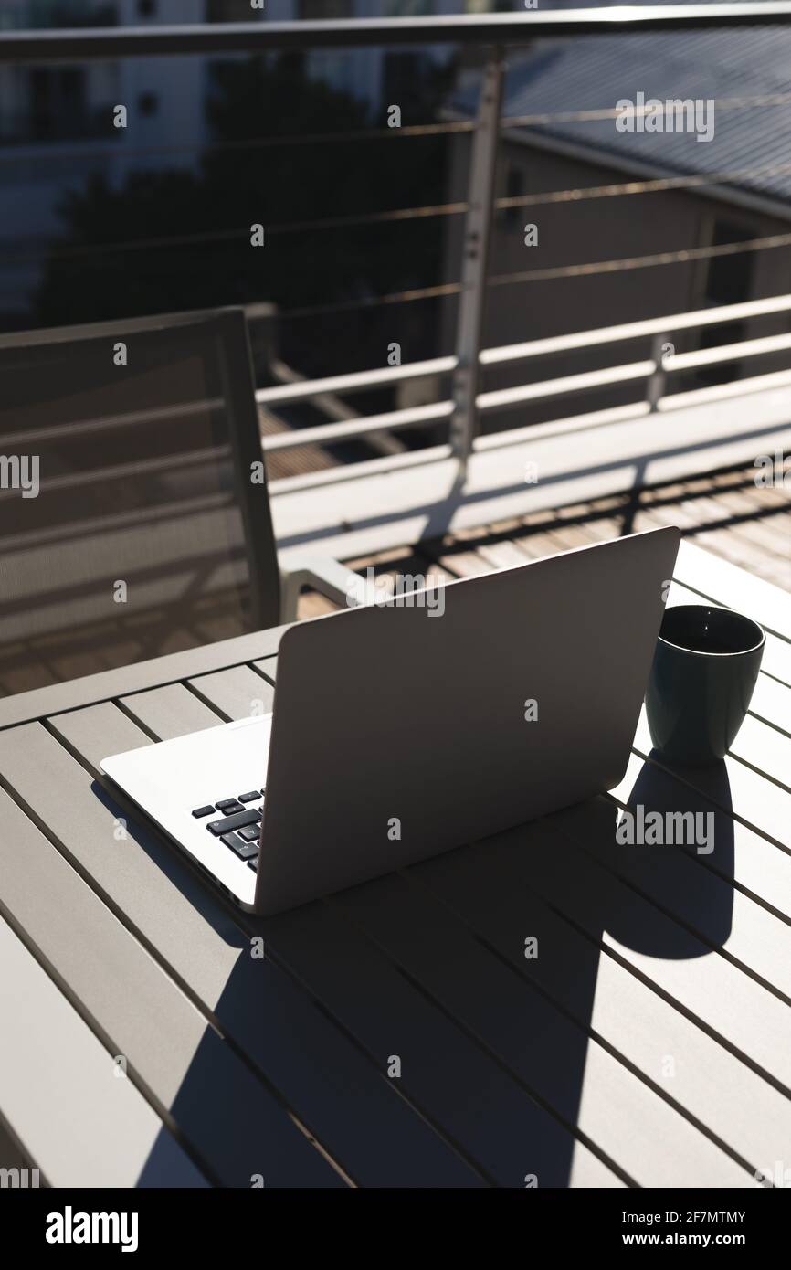 Laptop computer and coffee cup on table on sunny roof terrace Stock Photo