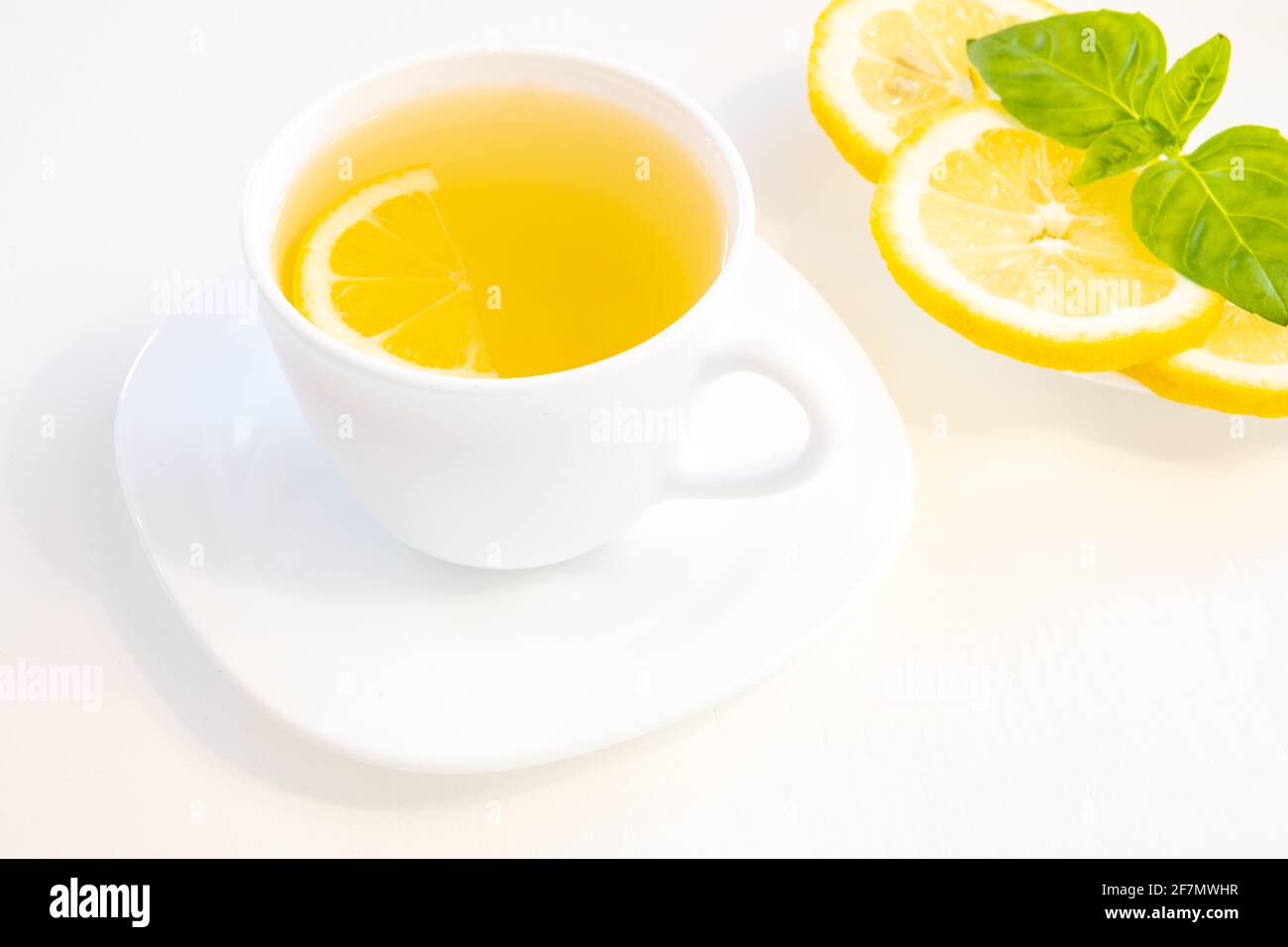 Cup of green tea with lemon slice, basil and mint isolated on white