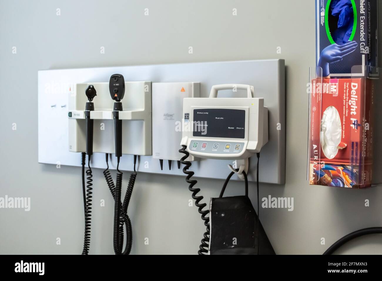 London, Ontario, Canada - February 26 2021 - Closeup of a hanging blood pressure monitor and a box of surgical gloves in a small family clinic. Stock Photo