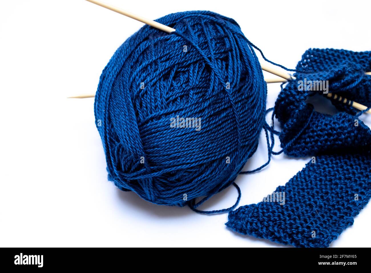 Midnight blue yarn, tangled and slightly astray next to beige knitting needles holding together a small classic pearl knit scarf. Stock Photo