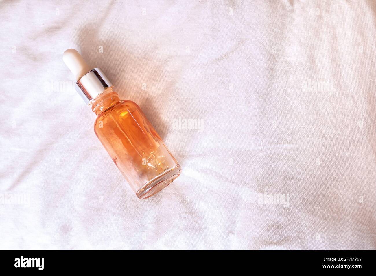An empty serum bottle with an orange tint and white dropper head, slightly unscrewed, on a white fabric, isolated, in Canada during the wintertime. Stock Photo