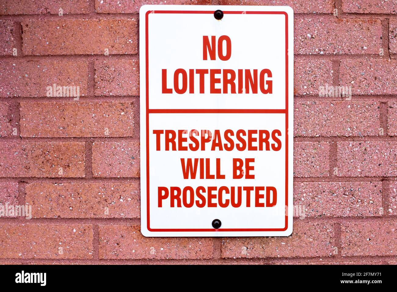 No loitering, trespasses will be prosecuted rectangular vertical sign drilled to a red brick wall in London, Ontario, Canada. Stock Photo