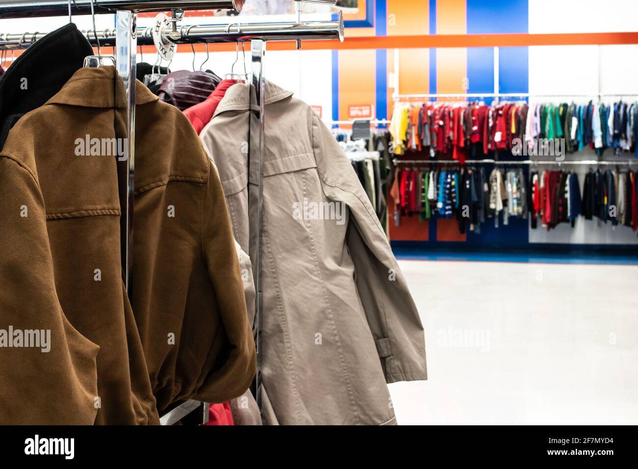 A suede jacket and a beige trench coat on a silver clothing rack in a thrift store in London, Ontario, Canada. Bokeh, soft-focus background. Stock Photo