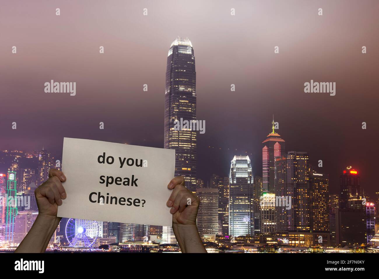 a man holding a sign in his hands and in the background the lights of the skyscrapers on Hong Kong Island Stock Photo