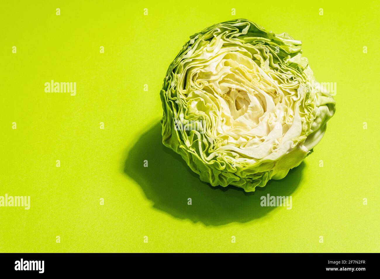 Fresh young cabbage, half a head in bright green background. Modern hard light, dark shadow