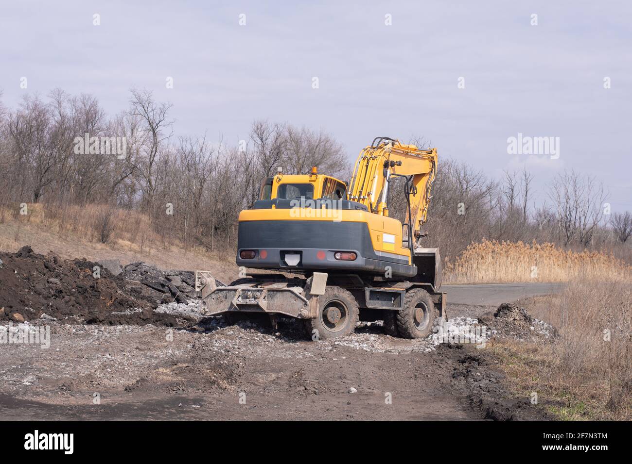 The yellow excavator works on road repairs.  Stock Photo