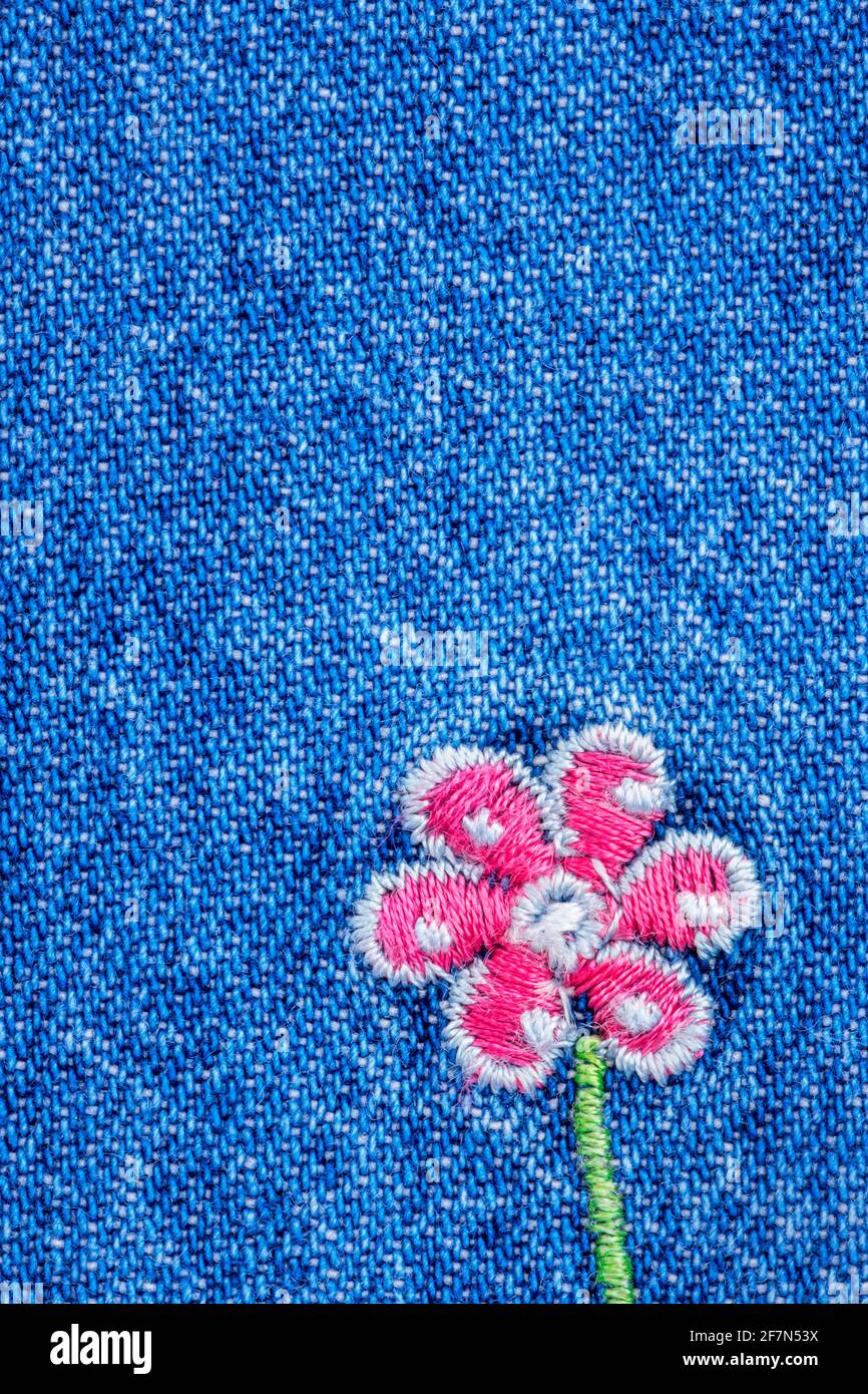 Embroidered pink flower on fragment of blue denim jeans texture Stock Photo