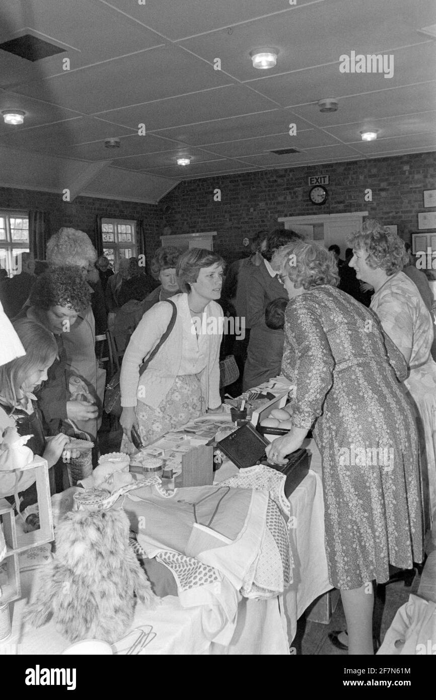 people looking at assorted second hand items for sale at traditional indoor church hall fete bring and buy jumble sale late 1970s uk Stock Photo