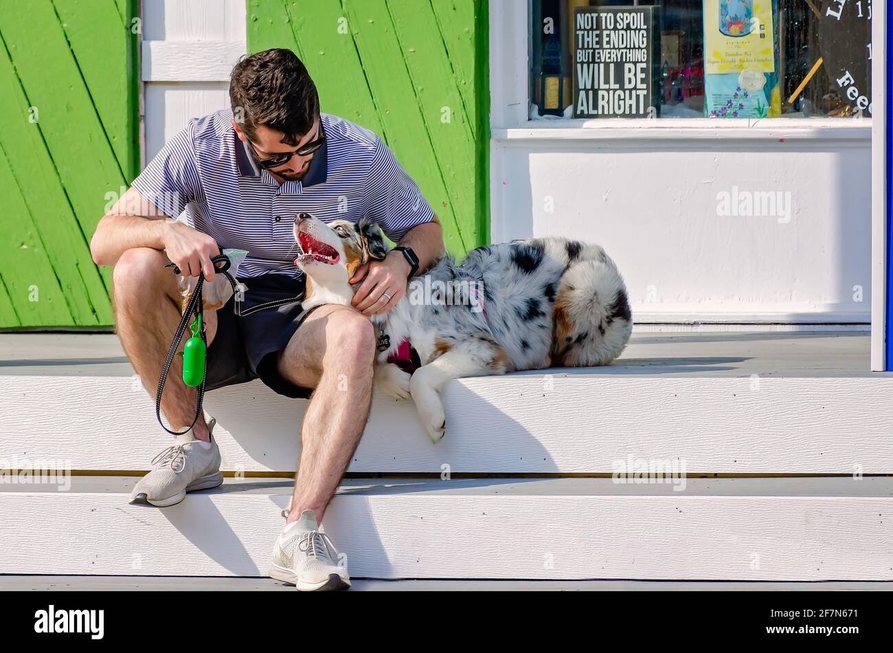 A man sits with his Australian Shepherd dog outside Social Chair, a boutique and gift shop, April 3, 2021, in Bay Saint Louis, Mississippi. Stock Photo