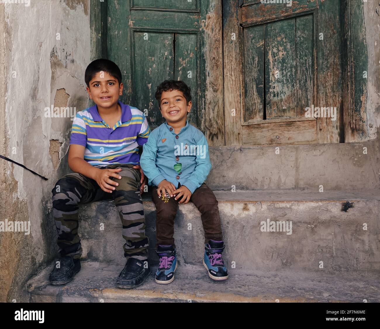 baghdad, Iraq - april 8, 2017:  two kids sitting on the old wood door Stock Photo