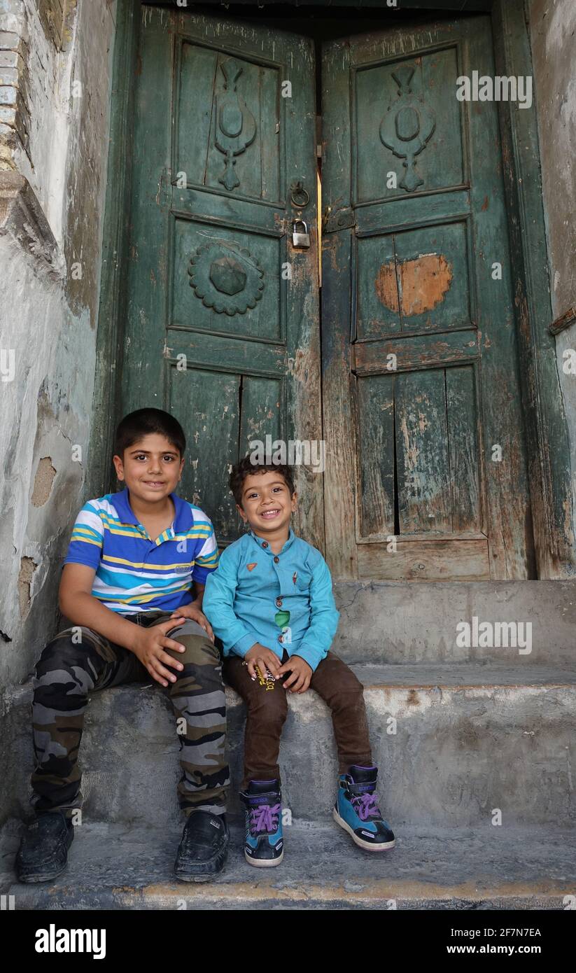 baghdad, Iraq - april 8, 2017:  two kids sitting on the old wood door Stock Photo