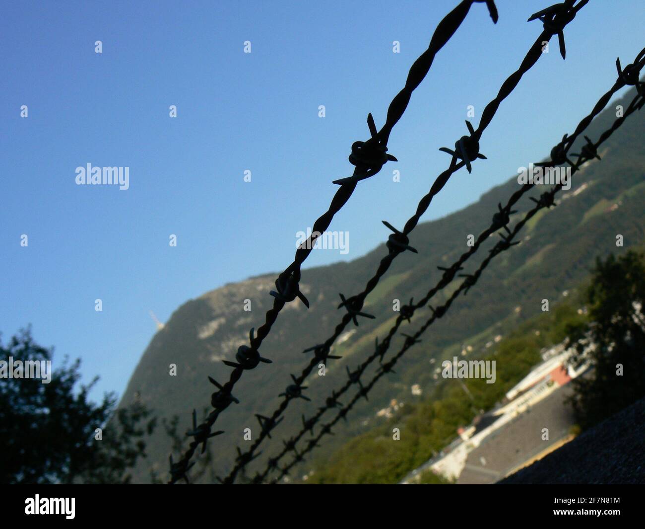 Dramatic silhouetted barbed wire fence against a bright blue summer sky; freedom and countryside in the distance - hills and forests Stock Photo
