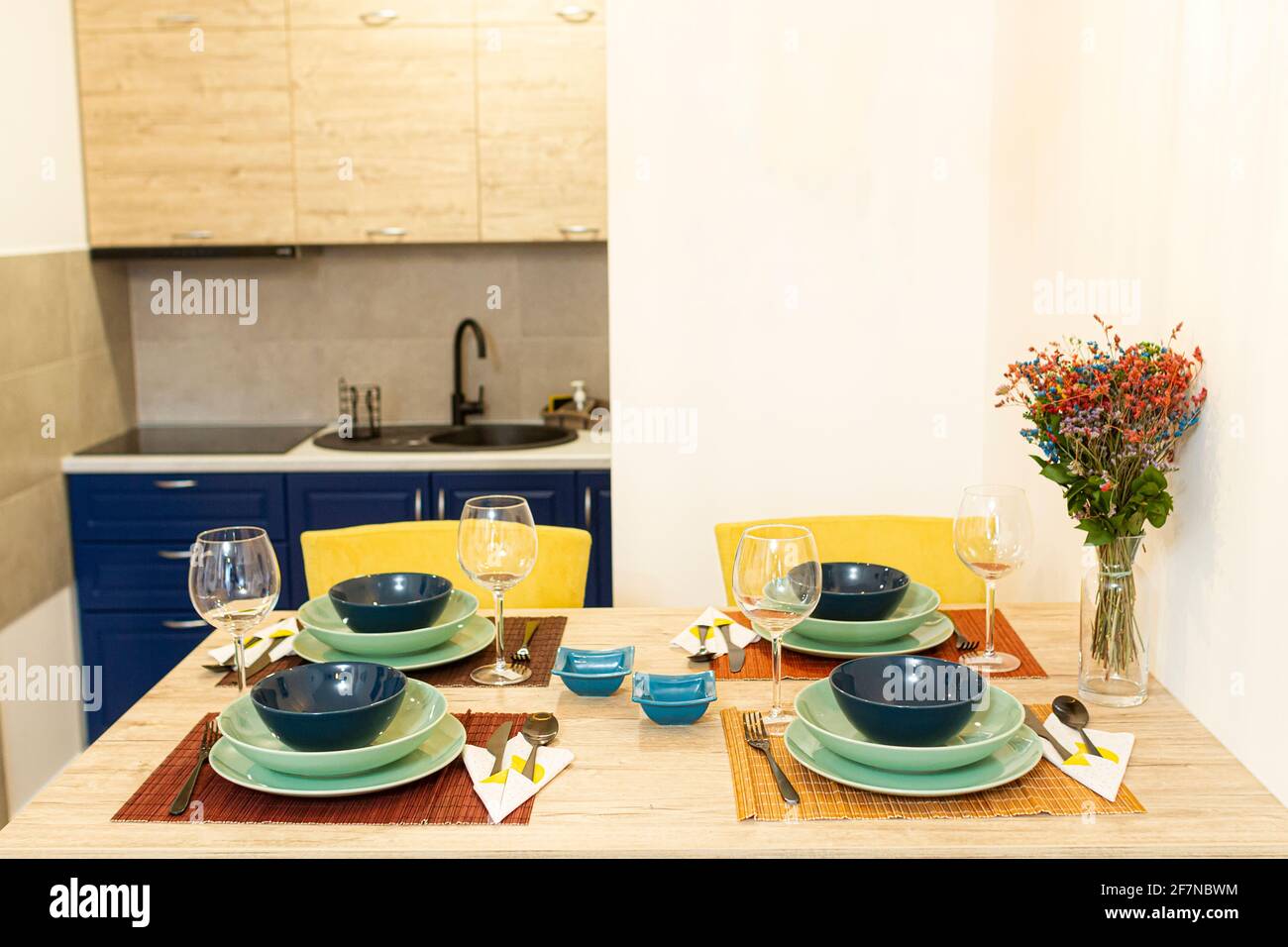 Wooden dining table in a modern dining room with a vase of plants, and a table set, ready to be served with food. Stock Photo