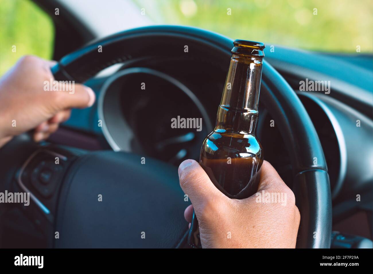 Closeup of drunk driver hands on the steering wheel with a bottle of