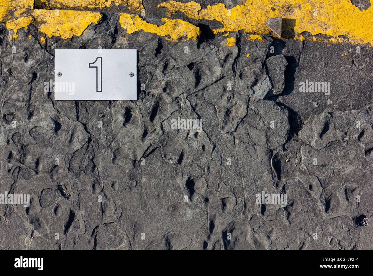 Asphalt background with a yellow strip on top and a white screwed-in tile with number one printed on it Stock Photo