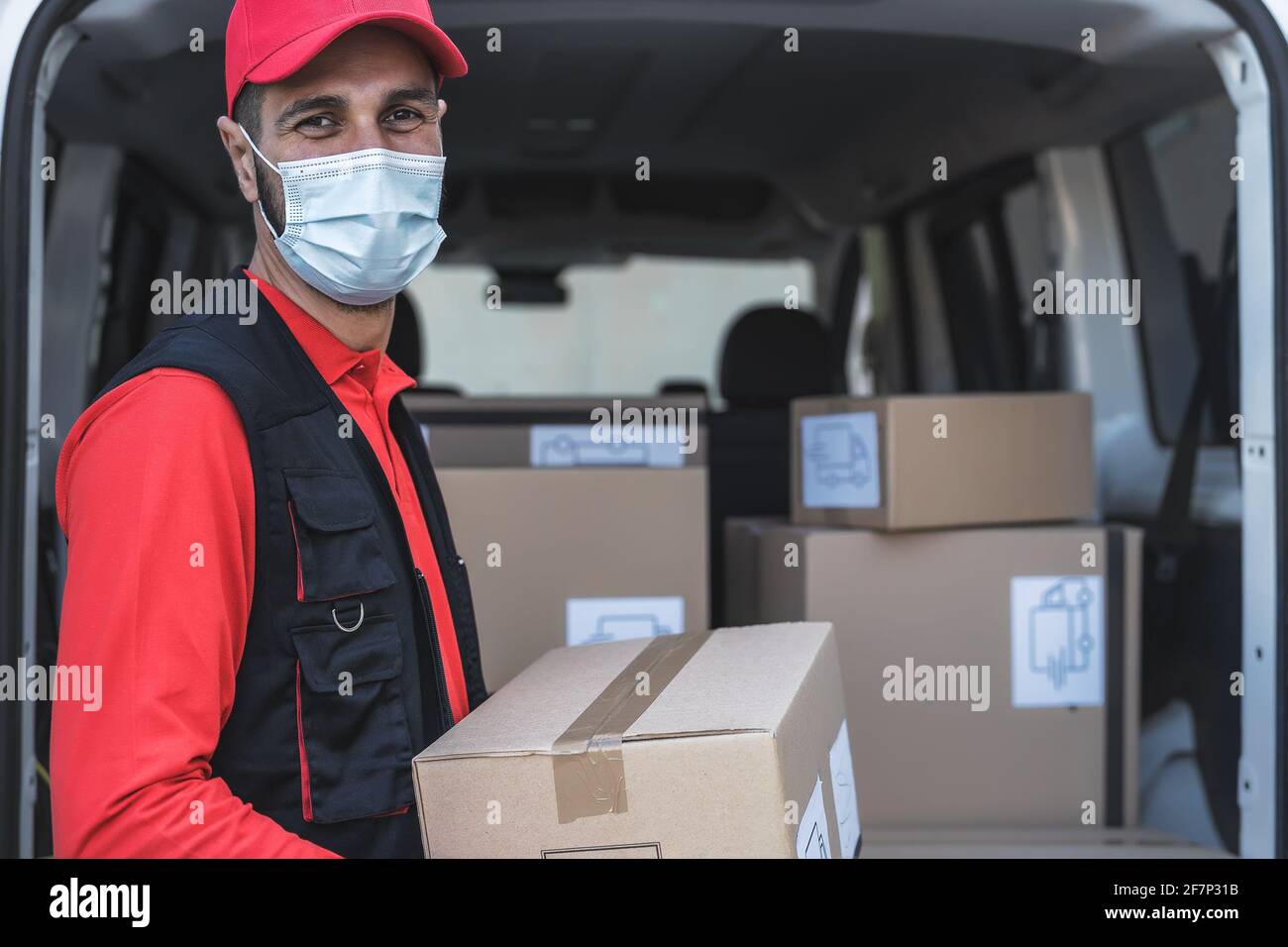 Young delivery man carrying cardboard box while wearing face mask to avoid corona virus spread - People working with fast deliver during corona virus Stock Photo