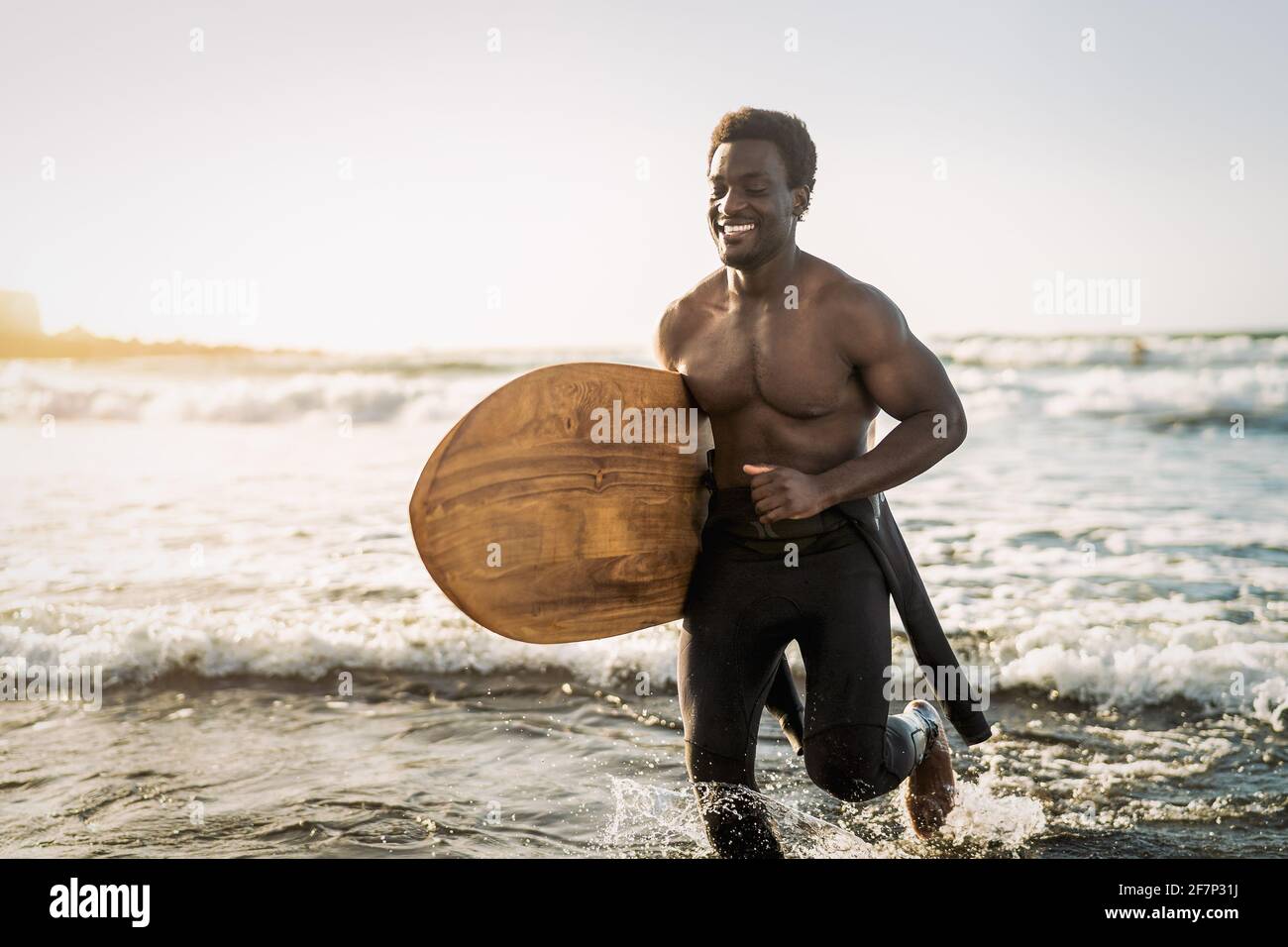 Male afro surfer having fun surfing during sunset time - African man enjoying surf day - Extreme sport lifestyle people concept Stock Photo