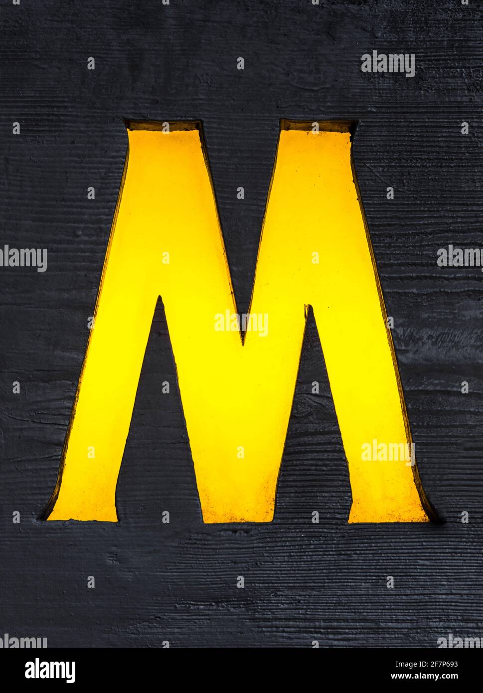 Yellow backlit letter M sawn out of a wooden board Stock Photo