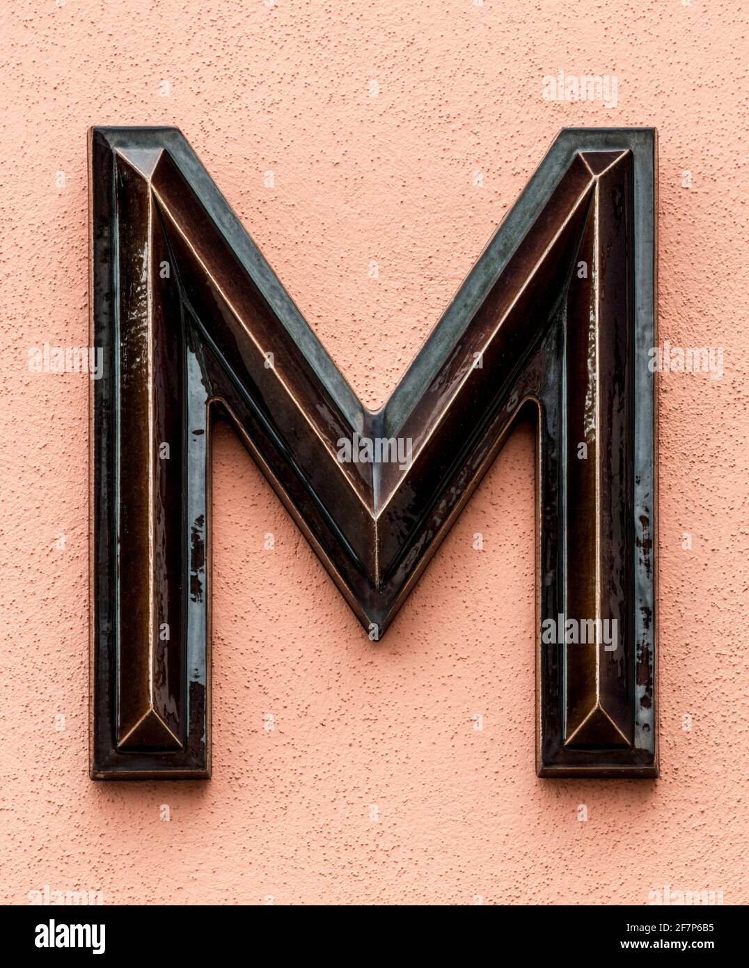 Dark brown glazed letter M on a bright orange wall Stock Photo