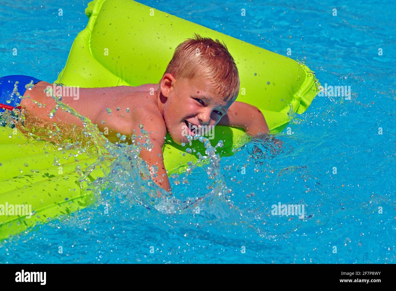 seven years old boy bathing in the swimming pool with an air mattress
