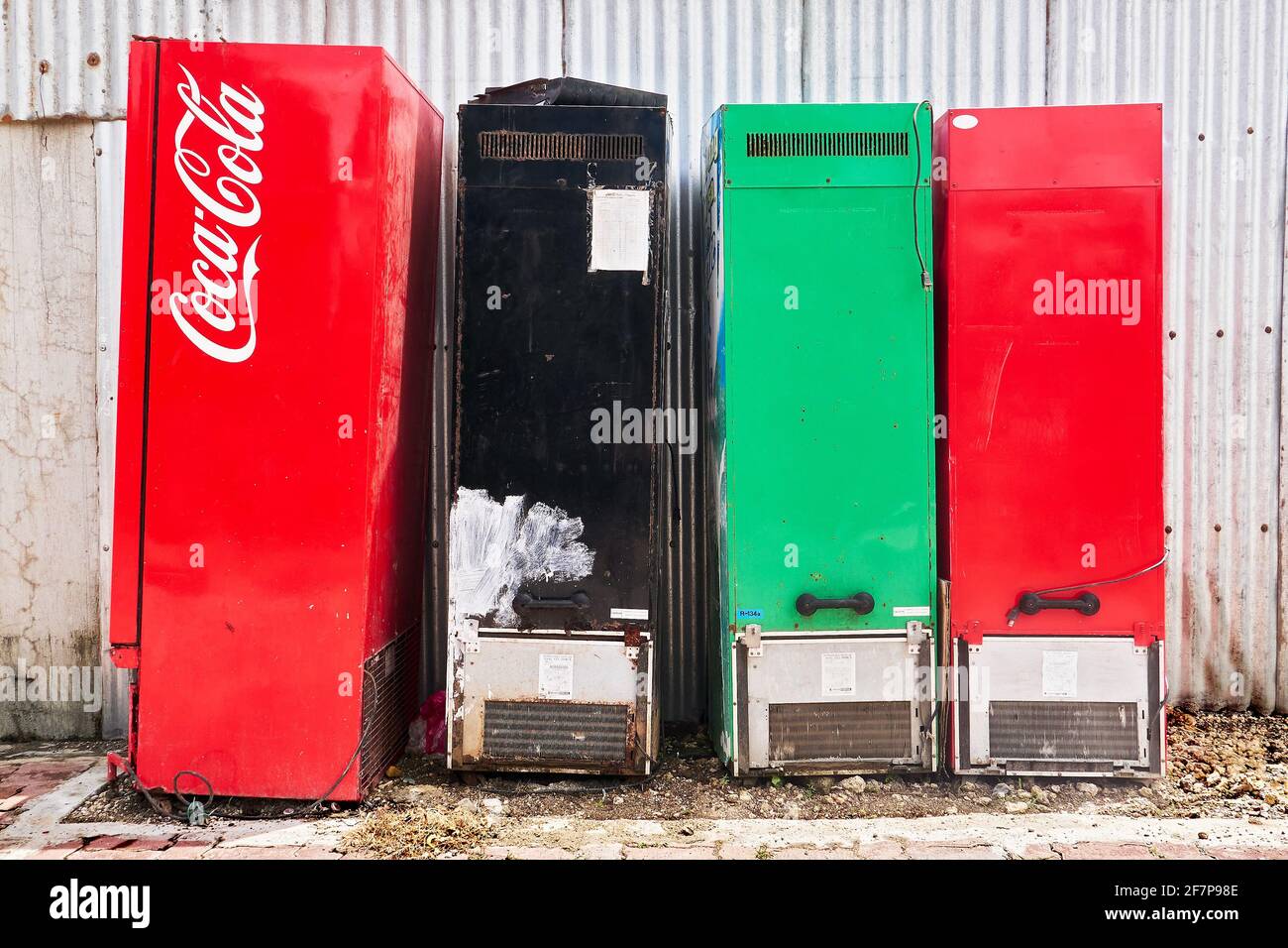 Close-up view of multicolored old and rusty refrigerators placed in a row next to a corrugated metal wall, seen along a road in the Philippines, Asia Stock Photo