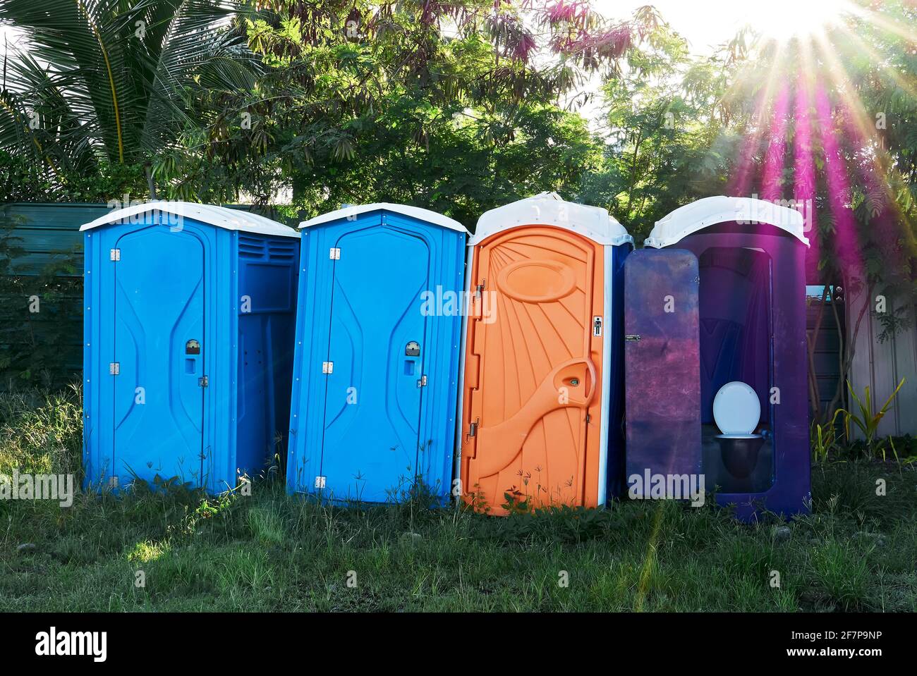 Four portable toilets standing in a row on a grassy public place in the Philippines, Asia, on a sunny summer day, with sun rays shining from above Stock Photo