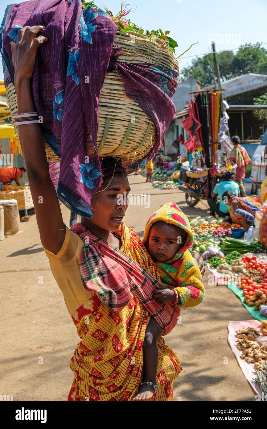 Koraput, India - February 2021: Adivasi woman from the Kondh tribe with her child shopping vegetables in the Koraput market on February 21, 2021 in Od Stock Photo