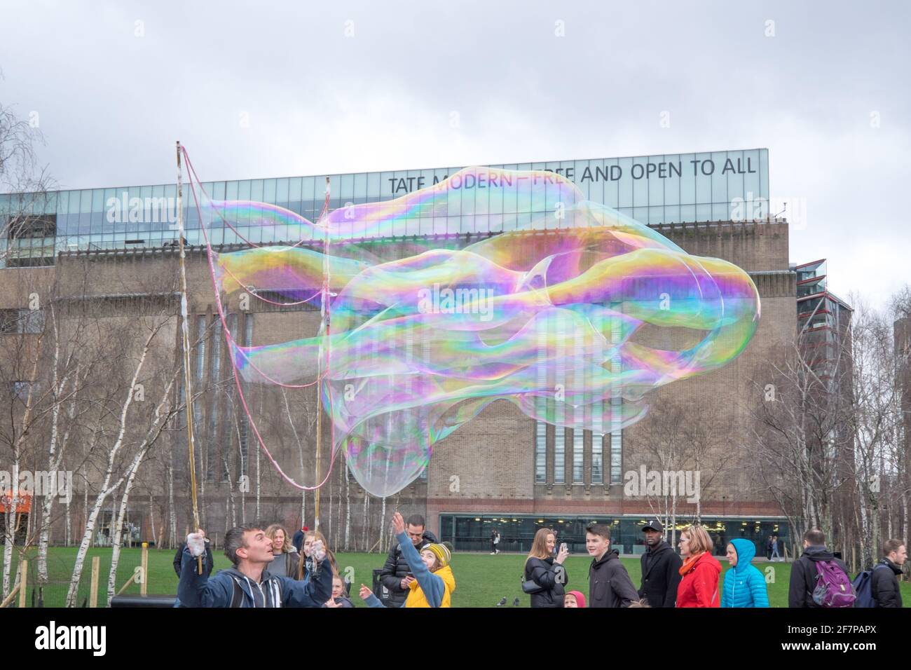 London, England, United Kingdom - March 15, 2020 - People entertained by man with giant bubbles outside Tate Modern Gallery for art on the South Bank Stock Photo