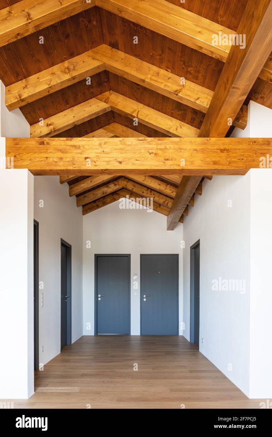 Front view hallway with exposed wood beams and closed doors, paquet floor and white walls. Nobody inside. Stock Photo