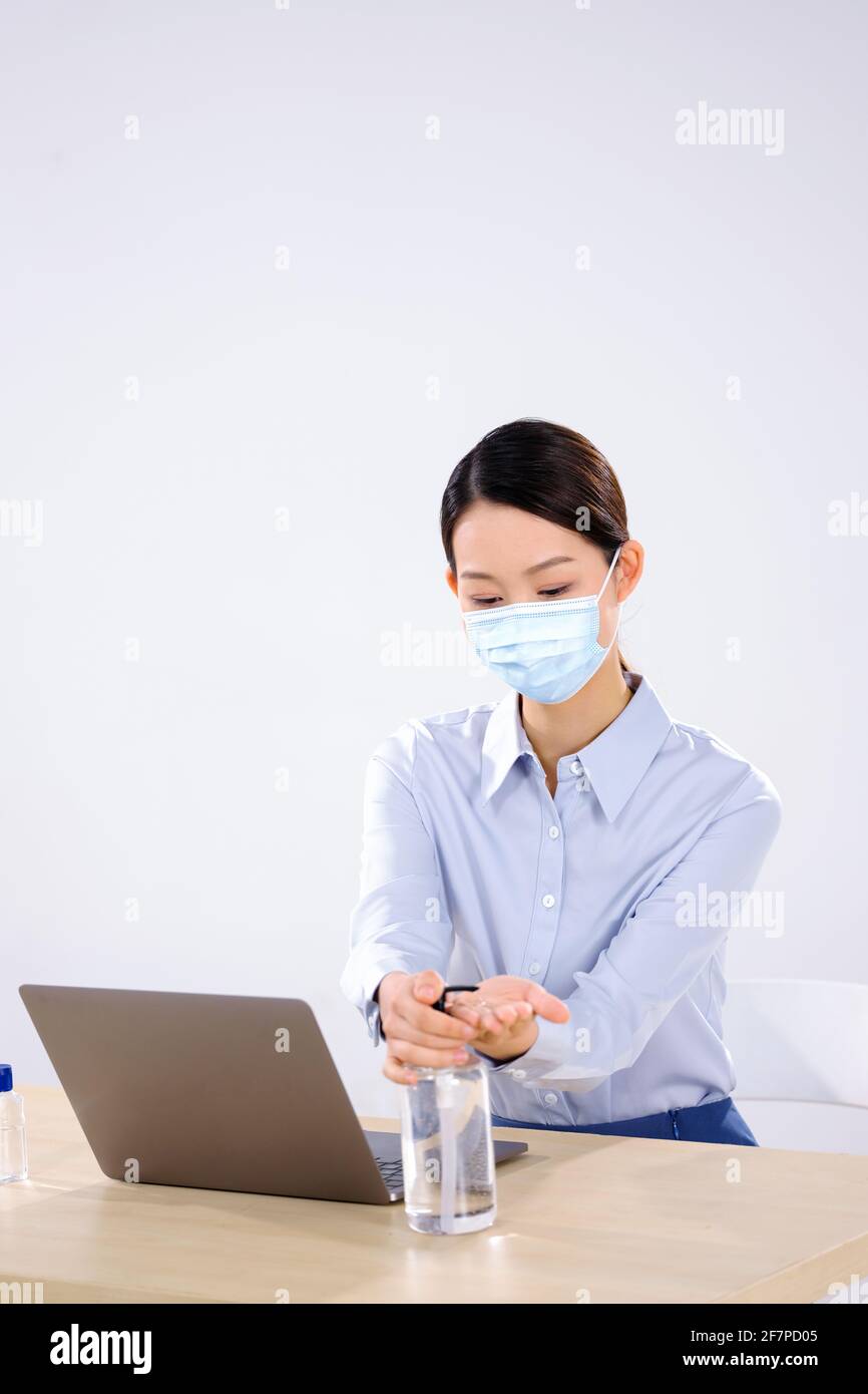 A business woman wearing a mask uses hand sanitizer side view Stock Photo