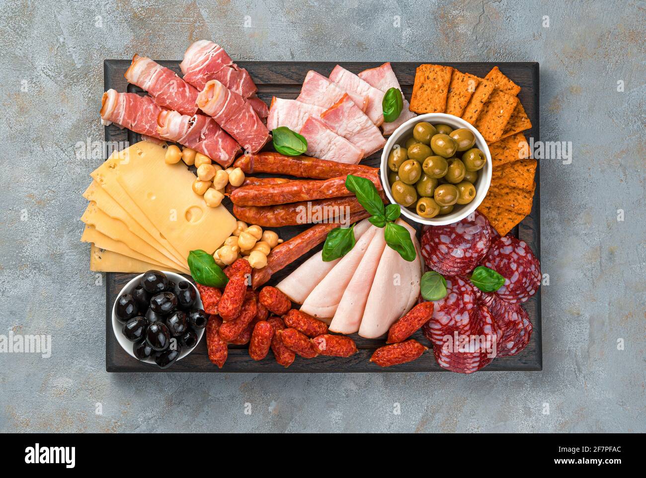 Meat appetizer, cheese and olives on a rectangular cutting board. Top