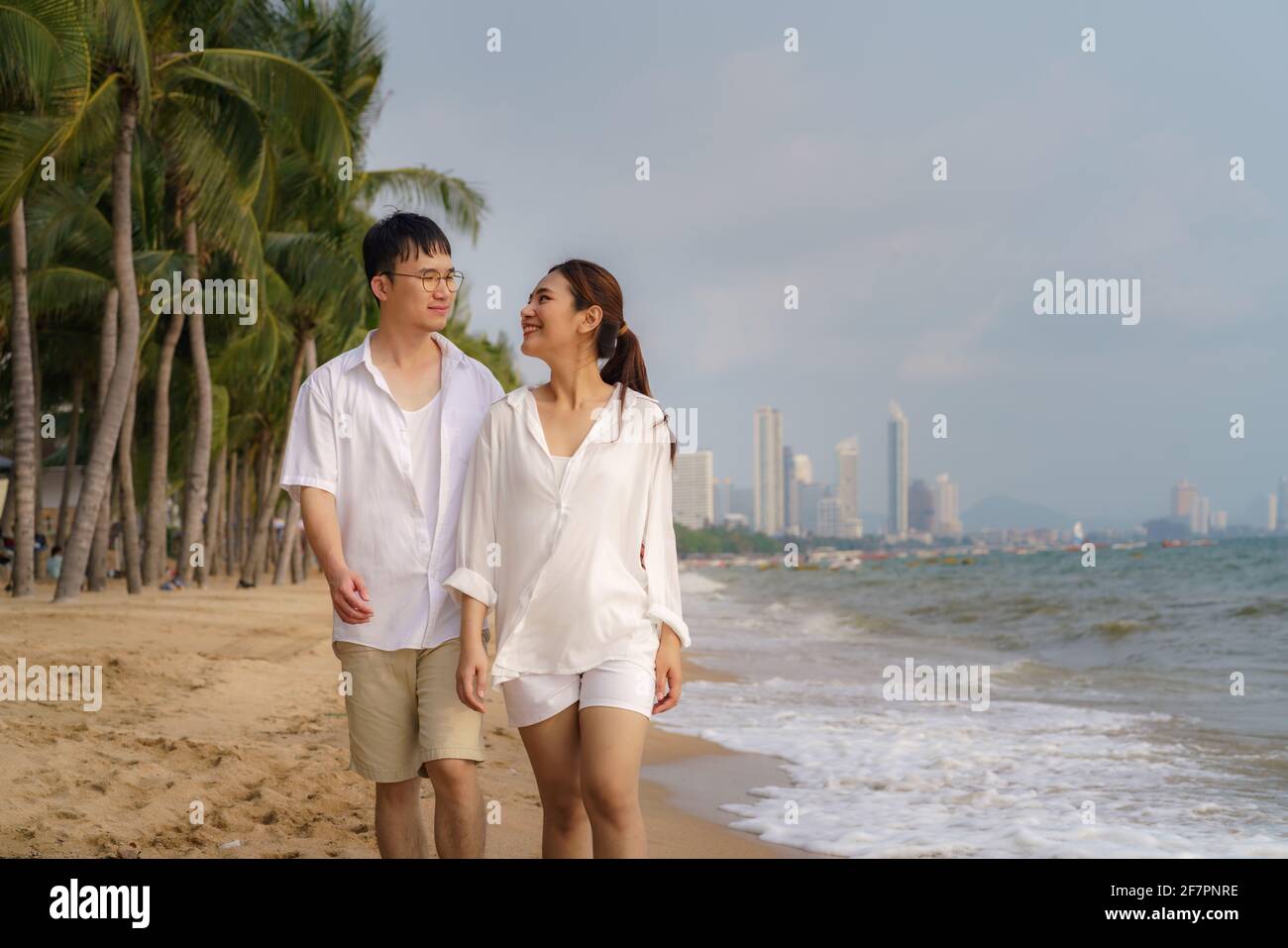 Asian couple is walking and hugging on a beachfront beach sea with coconut trees while on vacation in the summer in Thailand. Stock Photo