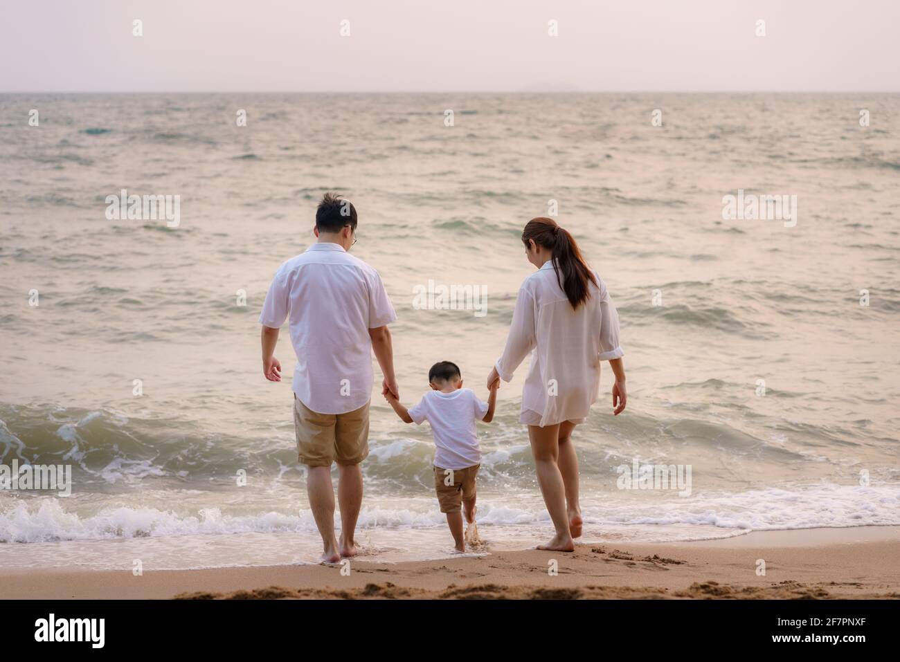 Asian family with fathers, mother and son are playing water sea along a beachfront beach with coconut trees while on vacation in the summer in Thailan Stock Photo