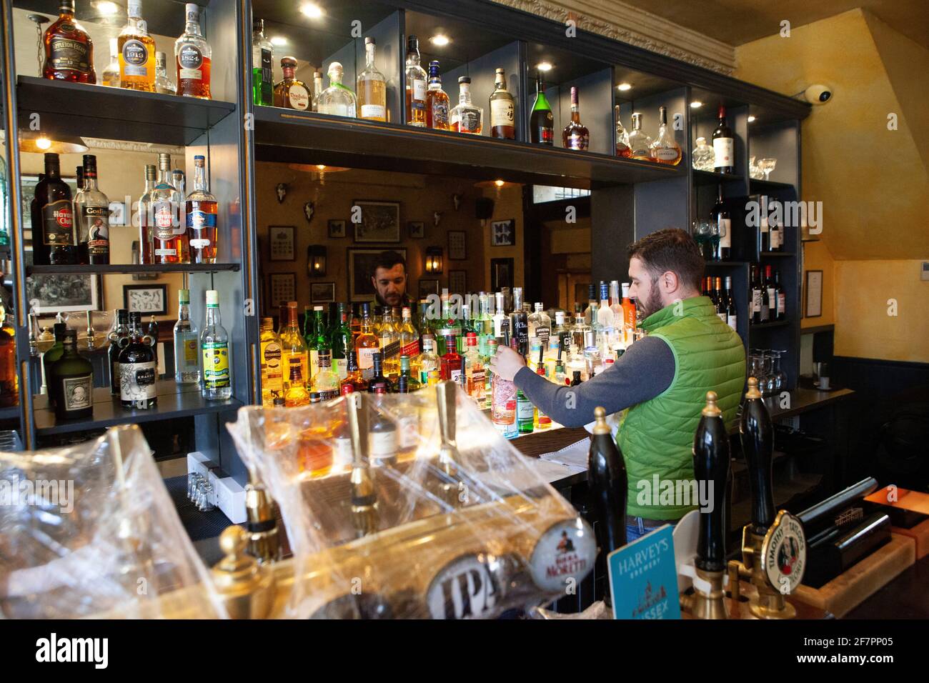London, UK, 9 April 2021: The Abbeville pub, in Clapham, gets ready for re-opening for outdoor drinks and dining on their terrace from 12th April. While the beer taps are kept clean under plastic wrapping, barman Klodian dusts bottles of spirits. Anna Watson/Alamy Live News Stock Photo