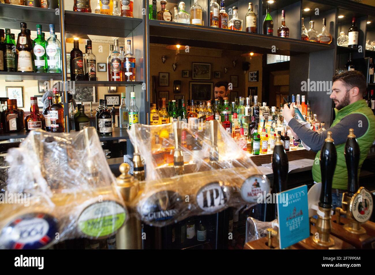 London, UK, 9 April 2021: The Abbeville pub, in Clapham, gets ready for re-opening for outdoor drinks and dining on their terrace from 12th April. While the beer taps are kept clean under plastic wrapping, barman Klodian dusts bottles of spirits. Anna Watson/Alamy Live News Stock Photo