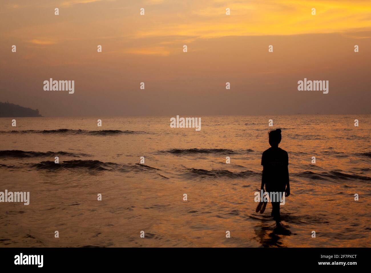 A silhouette of a girl in front of the sunset wadding in water in Goa,  India. The clouds are lit a yellow and shinning of the water Stock Photo -  Alamy