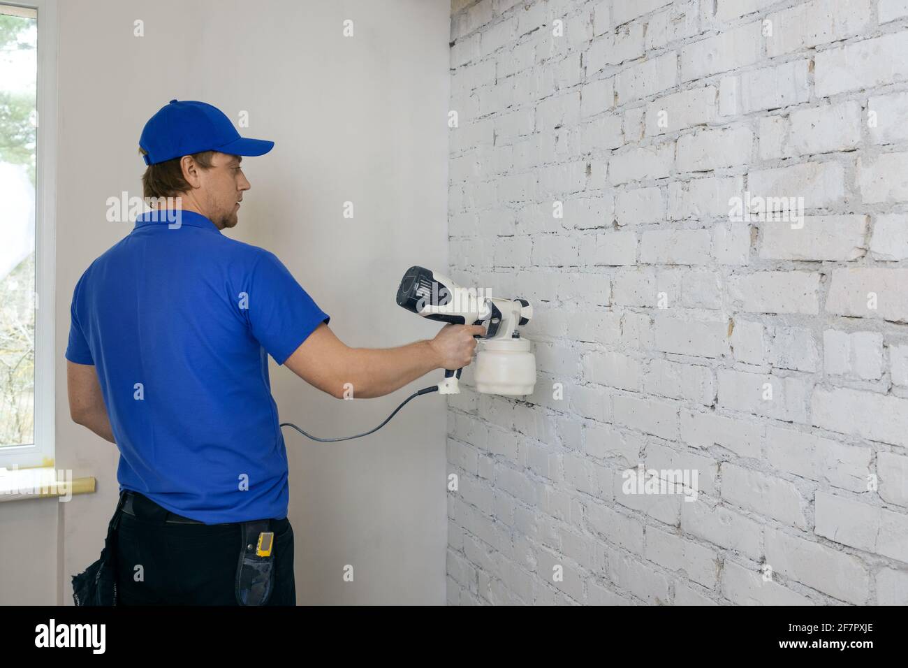 man painting old brick wall in white color with paint sprayer Stock Photo