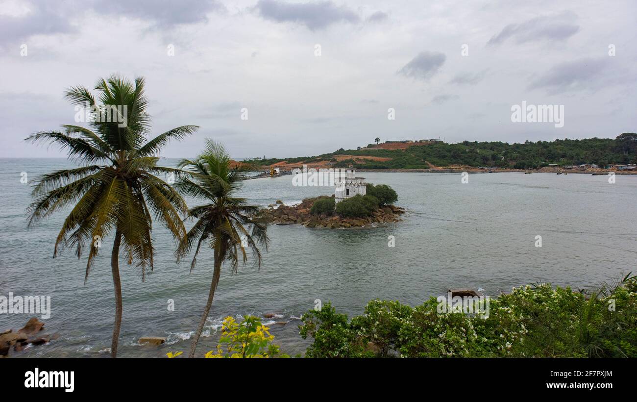 A lighthouse in a bay in Ghana, West Africa in a tropical landscape surrounded by trees and village. Stock Photo