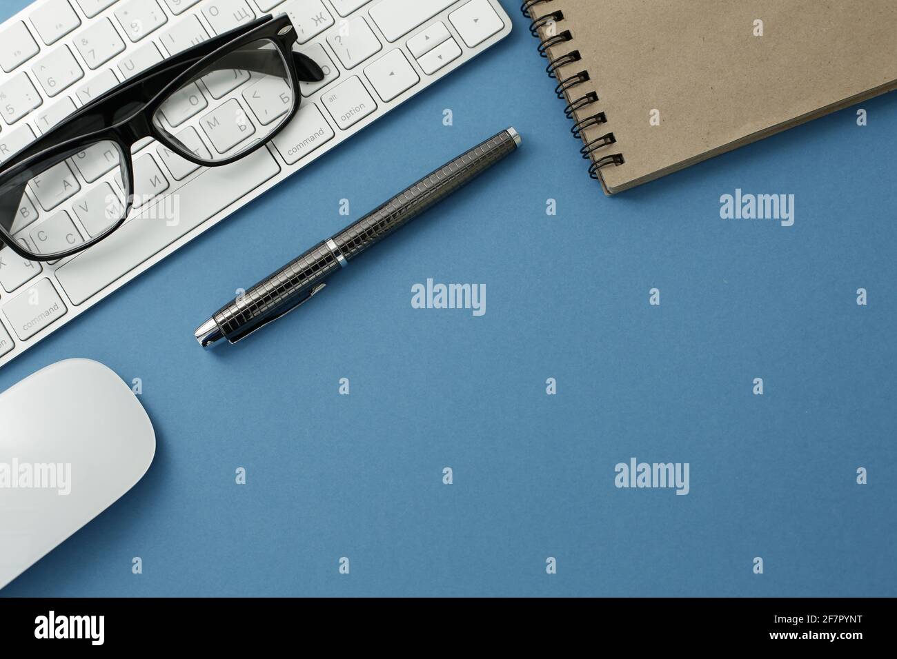 Glasses white keyboard notepad mouse and pen on blue background Stock Photo